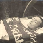 A dead Party member lies in his coffin, a banner across his chest instead of flowers.