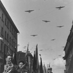 A band plays as part of a parade while a squadron of bombers flies by overhead (photograph by Ivan Shagin via Moscow House of Photography)